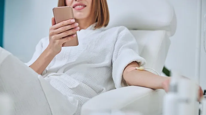 Young woman holding a mobile phone as beauty IV drips gain attention for glowing skin ahead of Navratri.